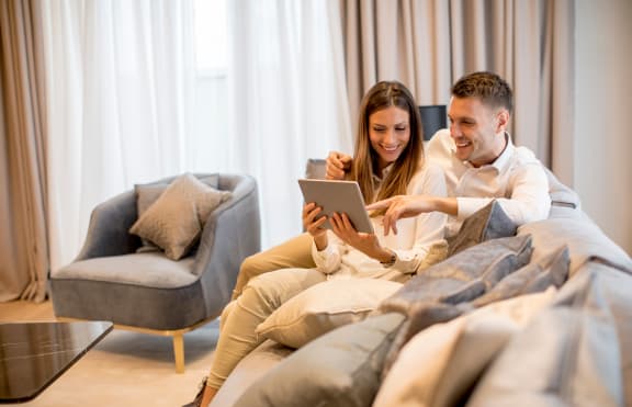 a man and woman sitting on a couch looking at a tablet