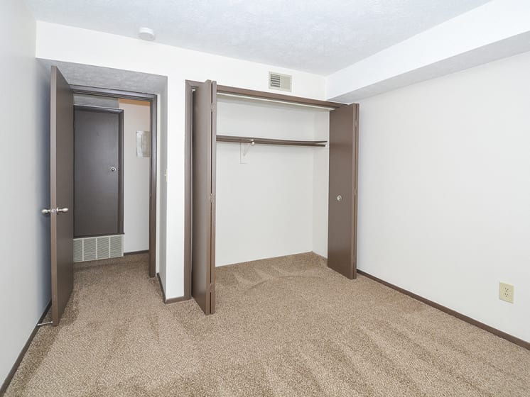 Carpeted Bedroom with Accordion Style Closet Doors and Brown Trim