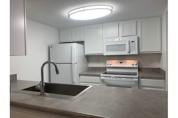 A kitchen with a sink, refrigerator, microwave, and oven.