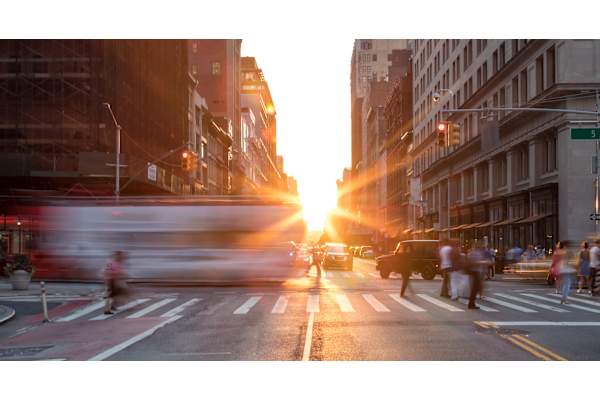 A busy city street at sunset with people crossing the road.