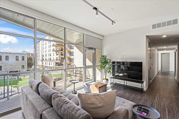 A modern living room with a grey sofa and a large window overlooking a cityscape. at Paperbox Lofts Apartments, Utah, 84101