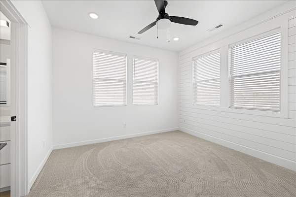 A room with a ceiling fan and two windows.