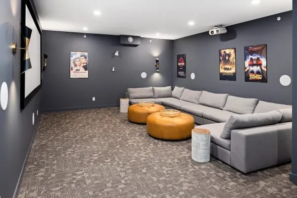 A living room with a grey couch, a yellow ottoman, and a patterned carpet.