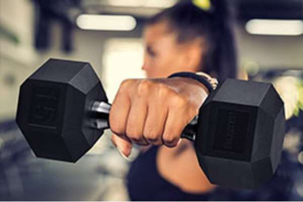 A woman is lifting a black dumbbell in a gym.