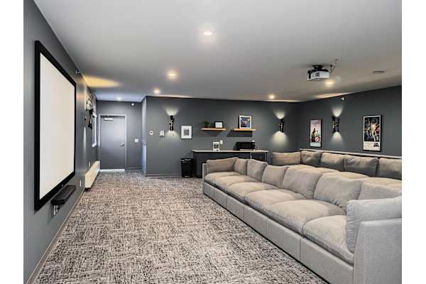 A spacious living room with a grey sofa and a large screen on the left side.