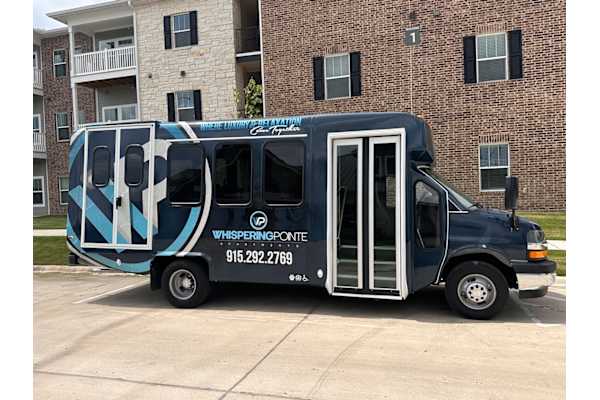 A blue and white truck with the words Whispering Ponde on the side is parked in front of a brick building.