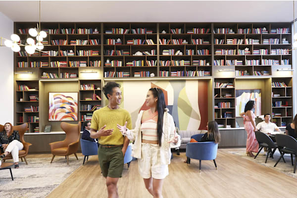 A man and woman are walking through a library with bookshelves in the background.