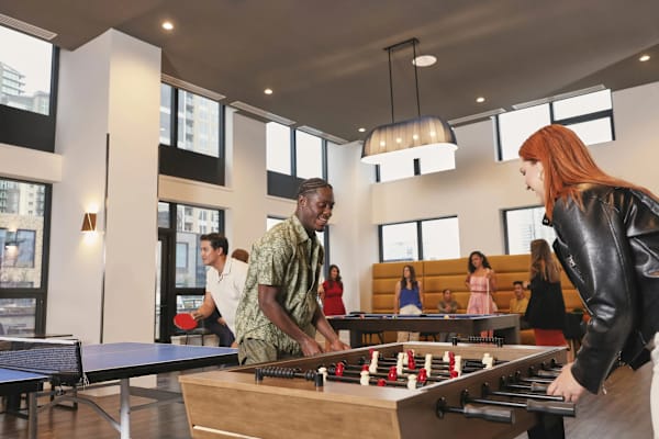 A man and a woman playing foosball in a room with people sitting in the background.