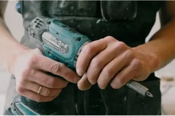 A person is holding a drill and a screwdriver.