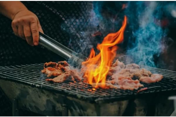A person grilling meat with flames and smoke.
