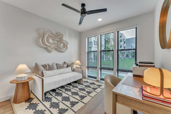 The Plaza at Pinnacle Hills living room with modern sofa and end table, floor to ceiling windows, work desk, ceiling fan and luxury plank flooring with area rug