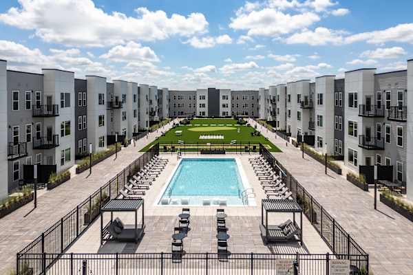 A swimming pool is surrounded by lounge chairs in a courtyard surrounded by apartment buildings.