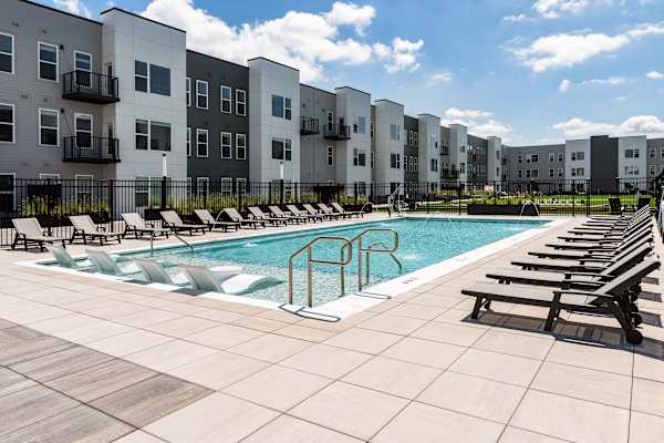 A swimming pool surrounded by lounge chairs and apartment buildings.