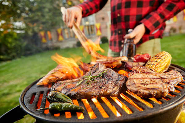 A person grilling various meats and vegetables on a barbecue.