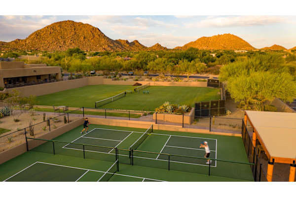 Two people playing tennis on a court with a mountain in the background.