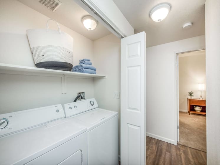 Full size washer-dryer behind bi-fold doors in main hallway and shelf above machines and wood plank floor