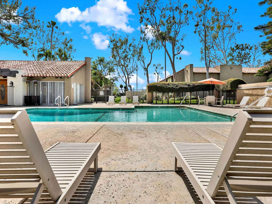 Two sun loungers sit on a poolside in front of a house.