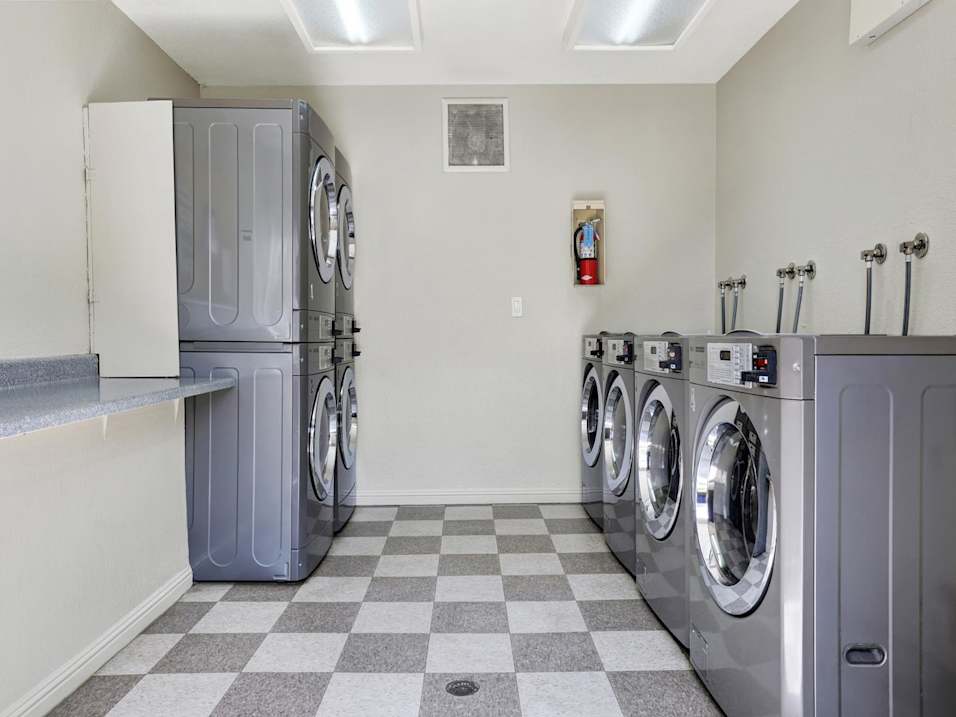 A laundromat with a checkered floor and a row of washers and dryers.
