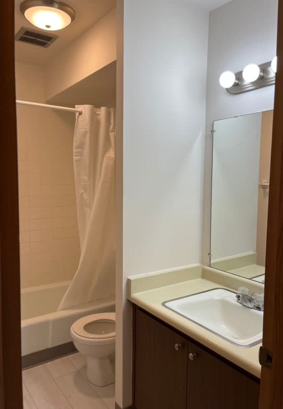 A white toilet is in a small bathroom with a sink and mirror.