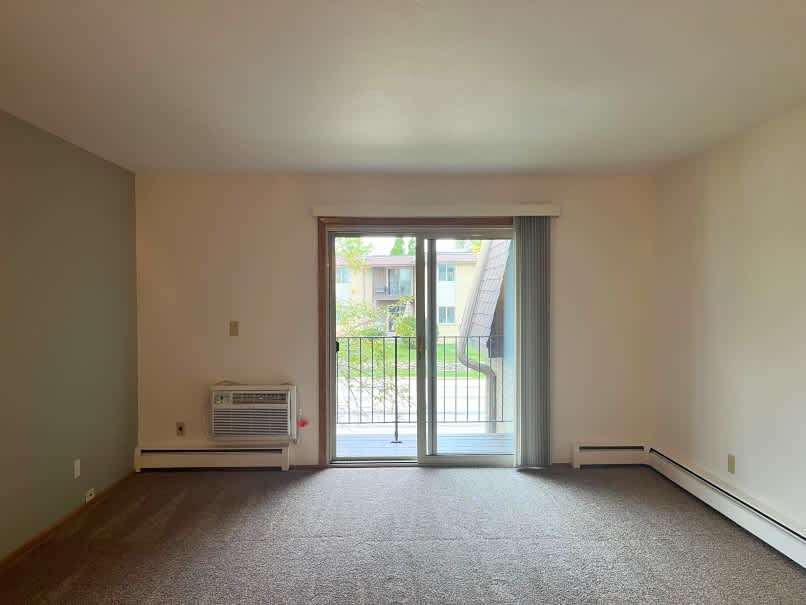 A room with a carpeted floor and a window with a view of a building outside.