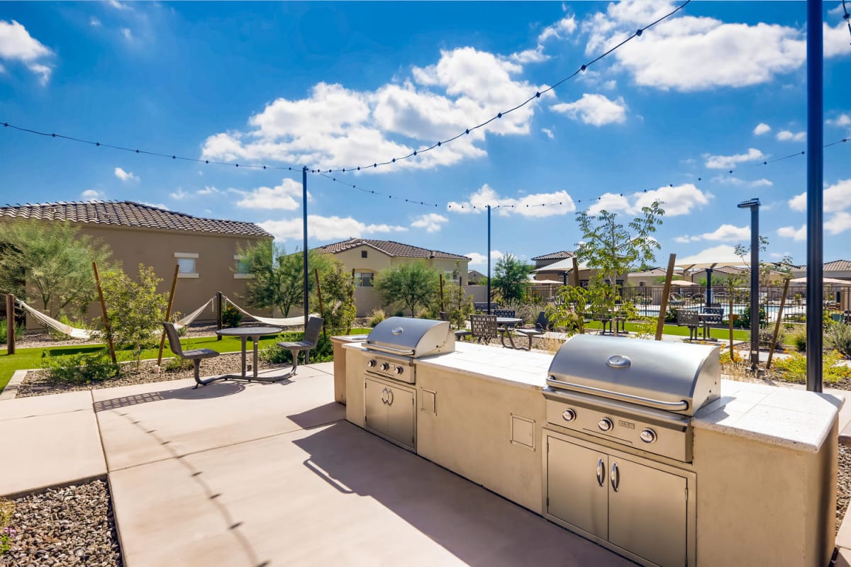 Outdoor grilling counter with two grills and nearby picnic seating.