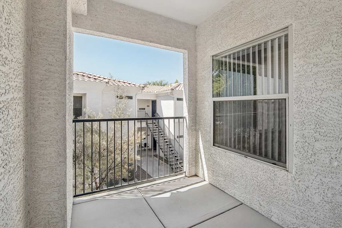 Covered balcony with a metal railing facing nearby apartments.