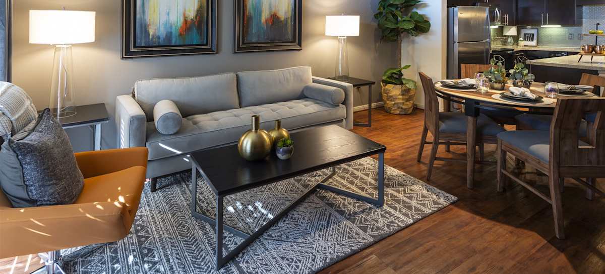 A furnished living room with a grey sofa, coffee table and the dining area behind it
