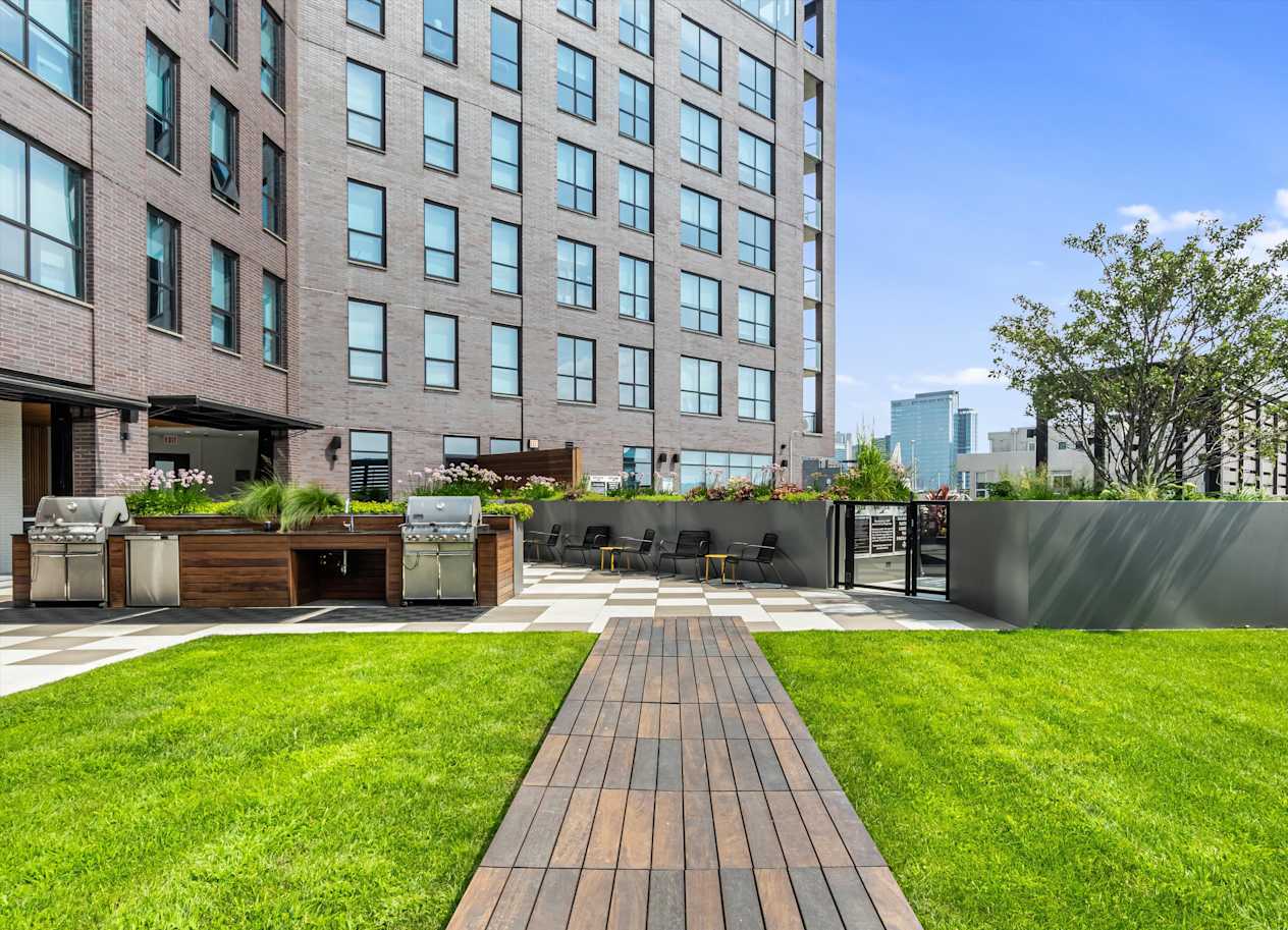 A large grassy area in front of a building with a wooden walkway leading to a seating area.