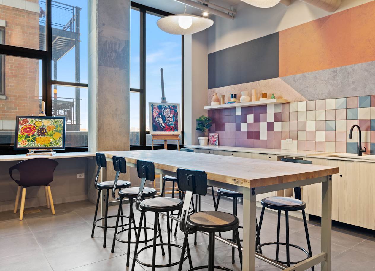 a communal table with chairs in a kitchen with large windows