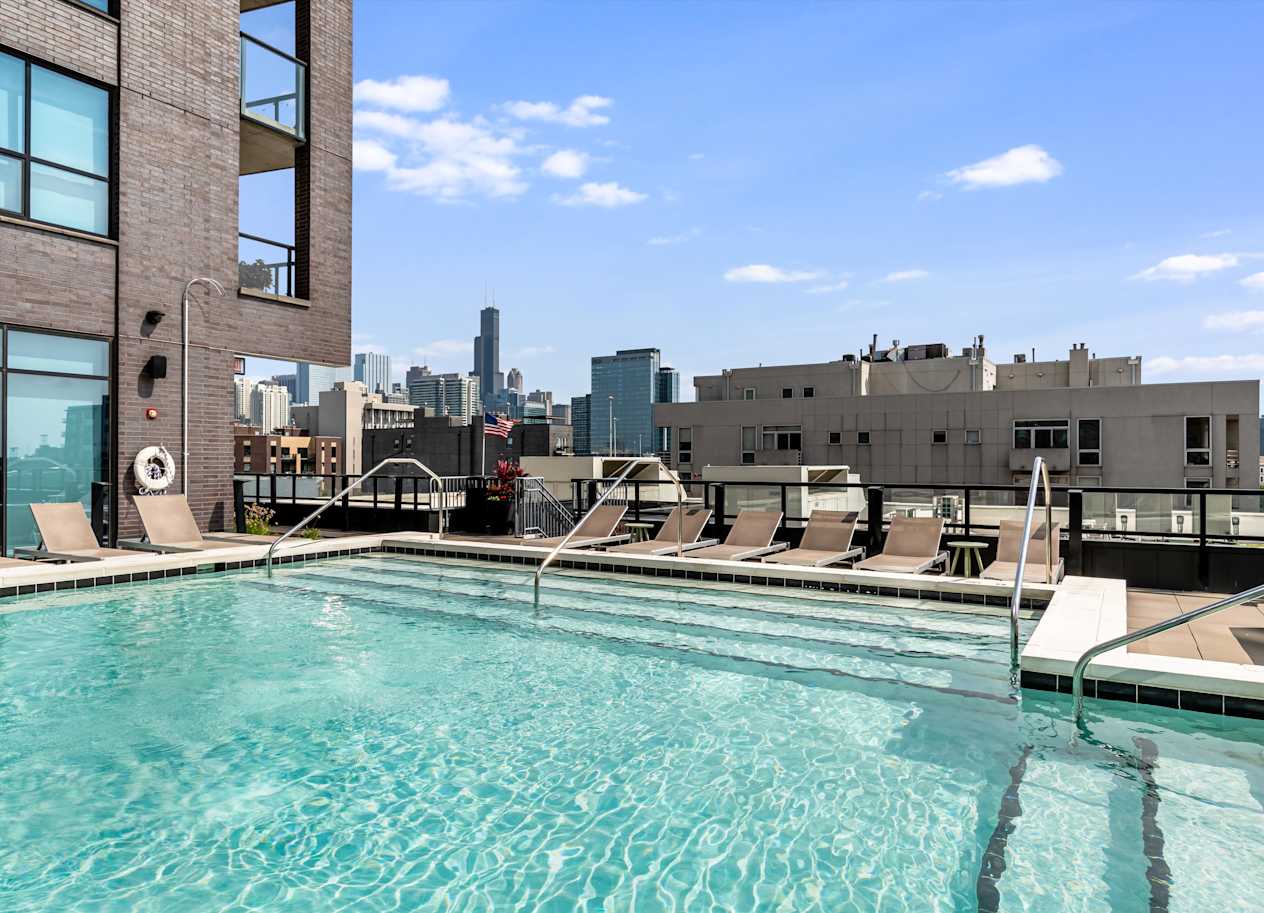 A swimming pool with lounge chairs and a city skyline in the background.