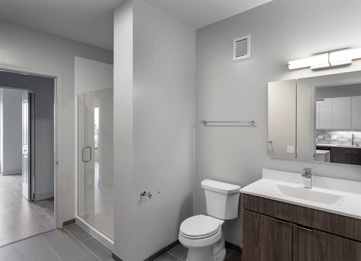 a bathroom with a toilet sink and mirror and a shower at Residences at Addison Clark Apartments, IL, 60613