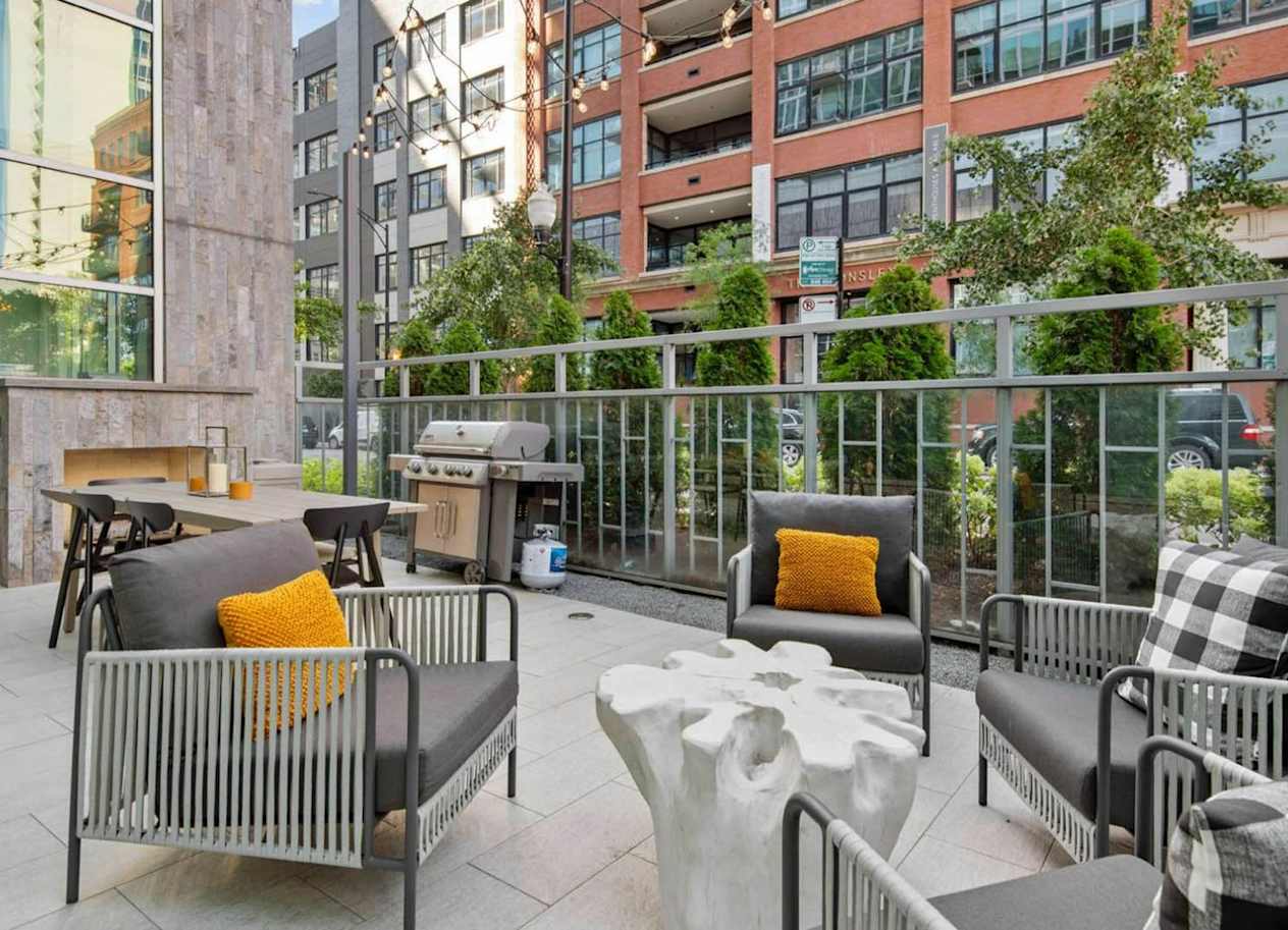 a patio with chairs and tables and a grill on the side of a building