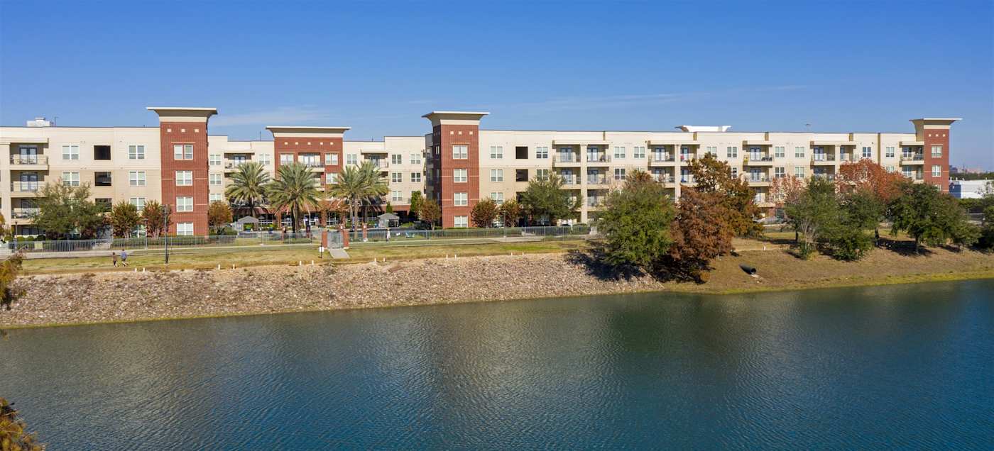 The lake in front of the buildings at Regard at Med Center, with trees along the bank