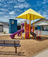 a playground with a yellow umbrella and a bench
