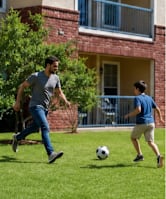 Two men playing soccer in front of a brick building.