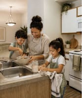 A woman and two children are washing dishes in a modern kitchen.