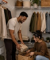 A man and a woman are in a room with clothes hanging on a rack.