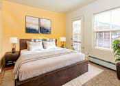 Thumbnail 8 of 19 - A bedroom with a bed, two lamps, a potted plant, and a painting on the wall.