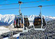 Thumbnail 7 of 10 - Two cable cars are suspended above a snowy mountain landscape.