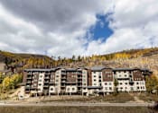 Thumbnail 2 of 10 - A large building with many windows is situated in front of a hill.