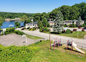 Thumbnail 9 of 9 - A playground with a slide and swings is surrounded by green grass and trees.