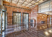 Thumbnail 6 of 74 - A marble hallway with a bench and a chandelier.