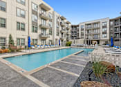 Thumbnail 2 of 39 - apartment building with a swimming pool and lounge chairs at LynnCora, Grand Prairie, Texas