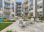 Thumbnail 4 of 39 - an outdoor patio courtyard with tables and chairs in front of an apartment building at LynnCora, Grand Prairie