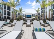 Thumbnail 4 of 79 - an outdoor pool lounge area with lounge chairs and tables and palm trees at Mira at Palmer Ranch in Sarasota, FL