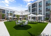 Thumbnail 10 of 79 - a courtyard with tables and umbrellas in front of a Mira at Palmer Ranch apartment building at Mira at Palmer Ranch in Sarasota, FL
