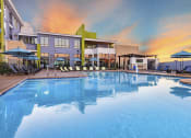 Thumbnail 7 of 23 - Resort style swimming pool with buildings and sunset in the background at Zeta Luxury Apartments in Sacramento, CA