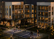 Thumbnail 5 of 15 - Three people playing tennis on a court in front of a building.