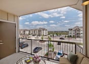 Thumbnail 15 of 30 - A balcony with a table and chairs overlooking a parking lot and other houses.