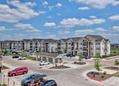 Thumbnail 2 of 35 - A red car is parked in a parking lot in front of apartment buildings.